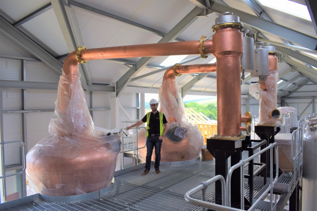 Josh Office Manager beside new stills at GlenWyvis Distillery